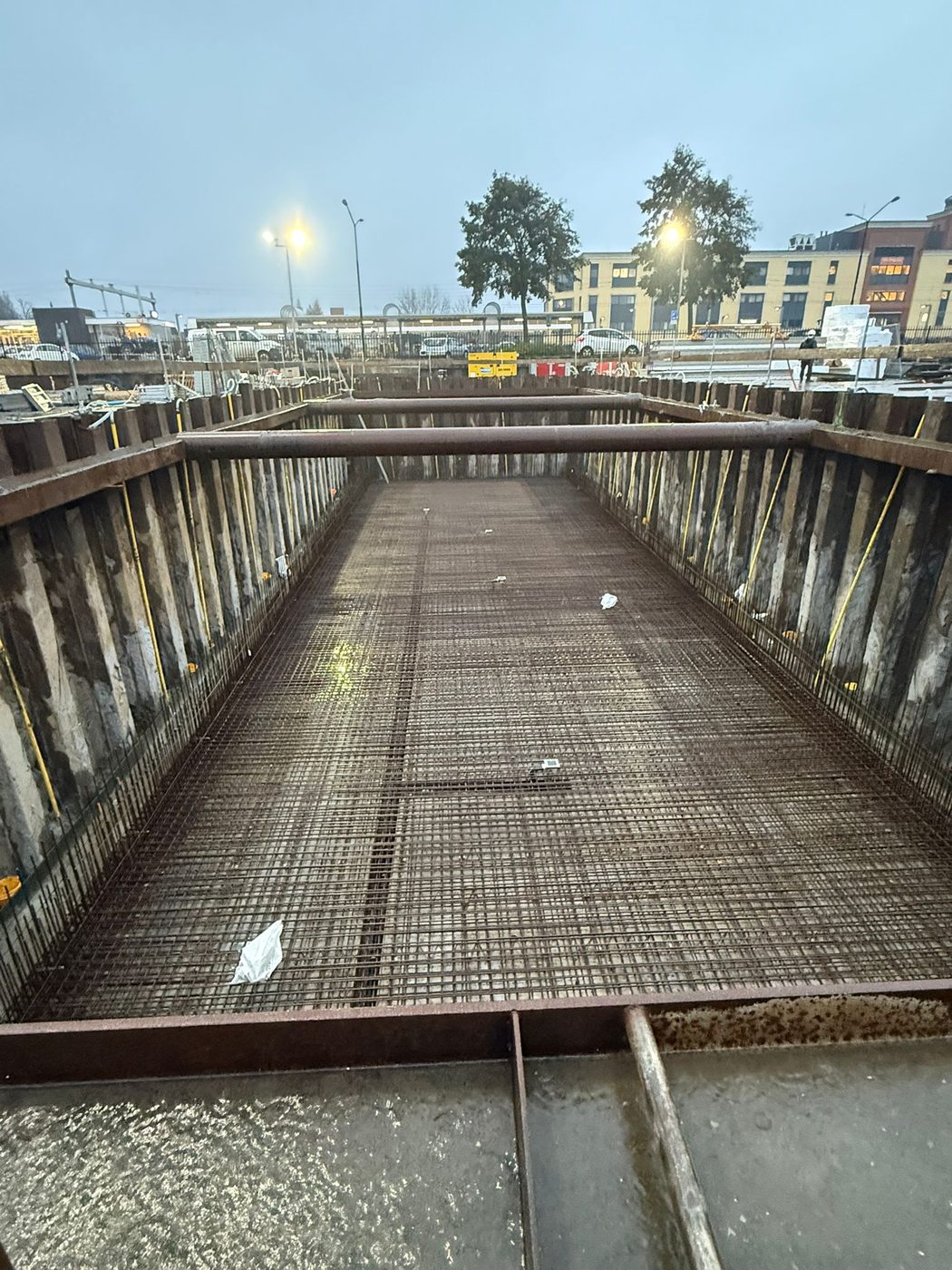 De bouwkuip bij avondlicht, met de gewapende keldervloer tussen de damwanden