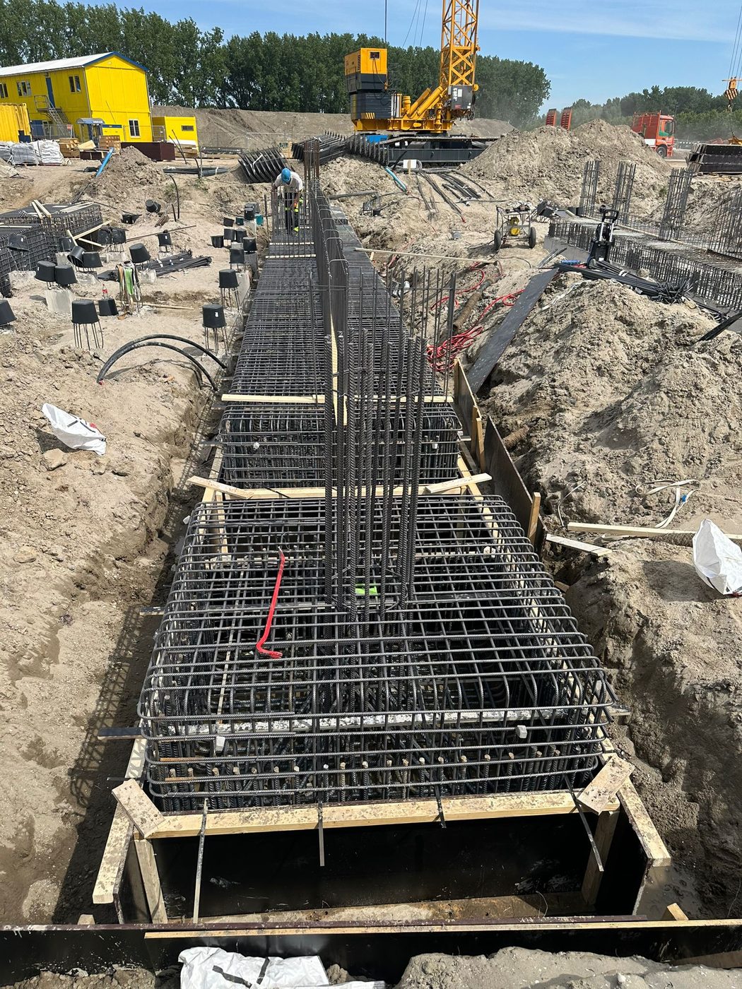 Wapening van een funderingsbalk in de sleuf, met de torenkraan op de achtergrond