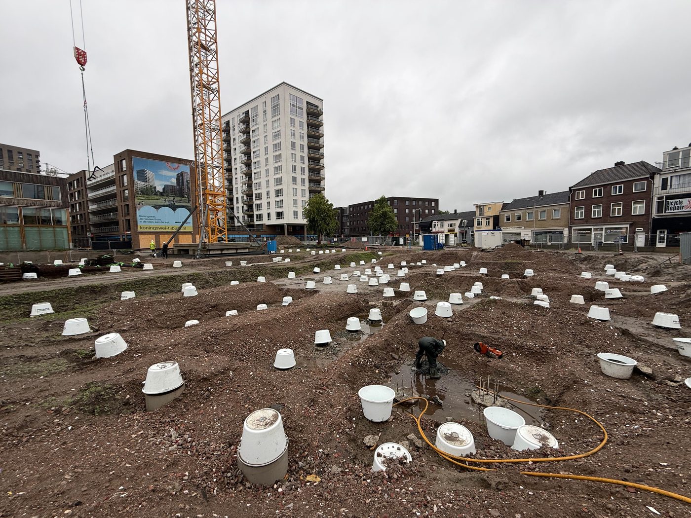 Overzicht van de bouwplaats met paalkoppen en torenkraan, gezien vanaf de Koningswei