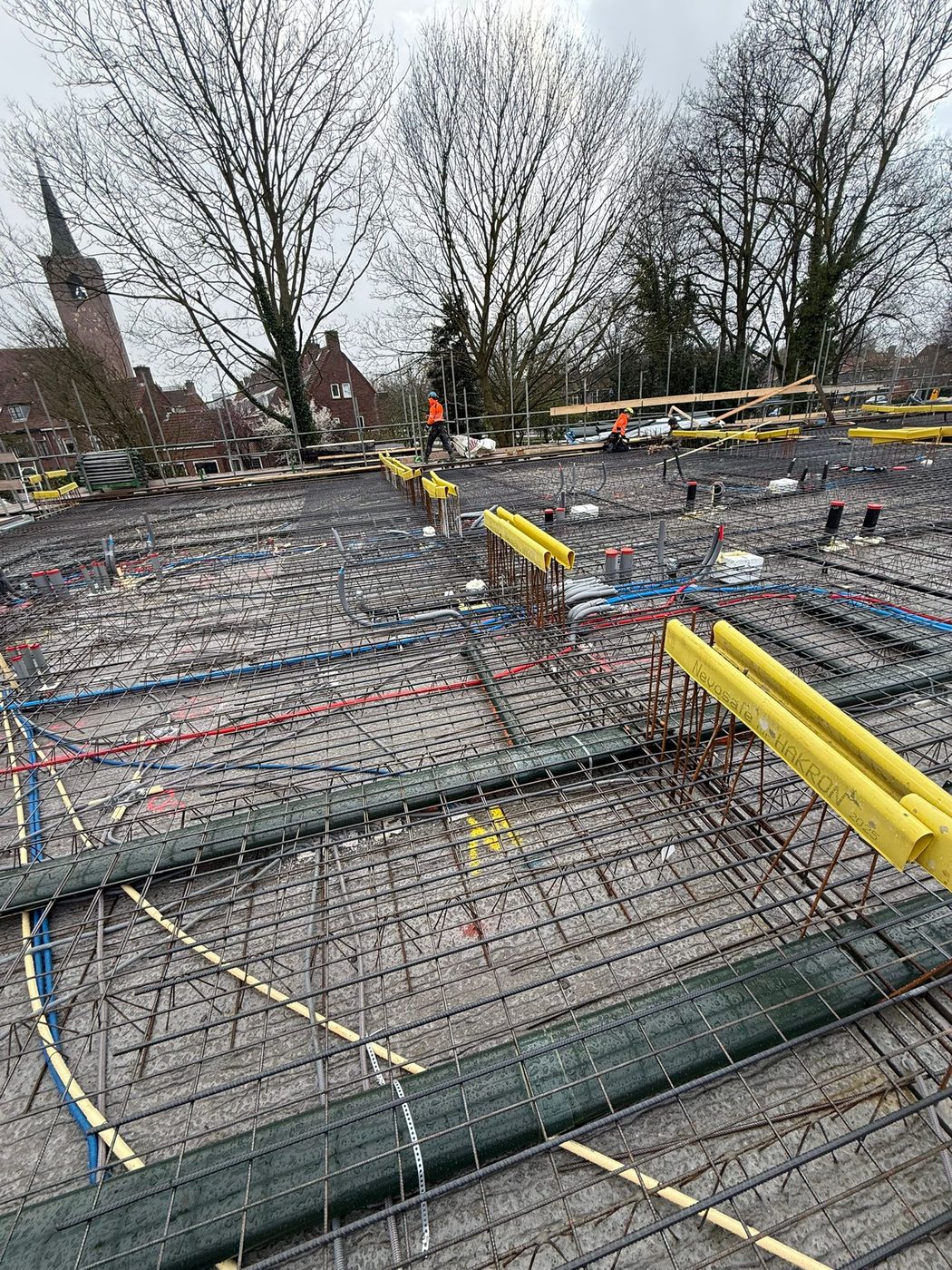 Funderingsvloer met het ingepaste leidingwerk, met de kerktoren van de wijk op de achtergrond